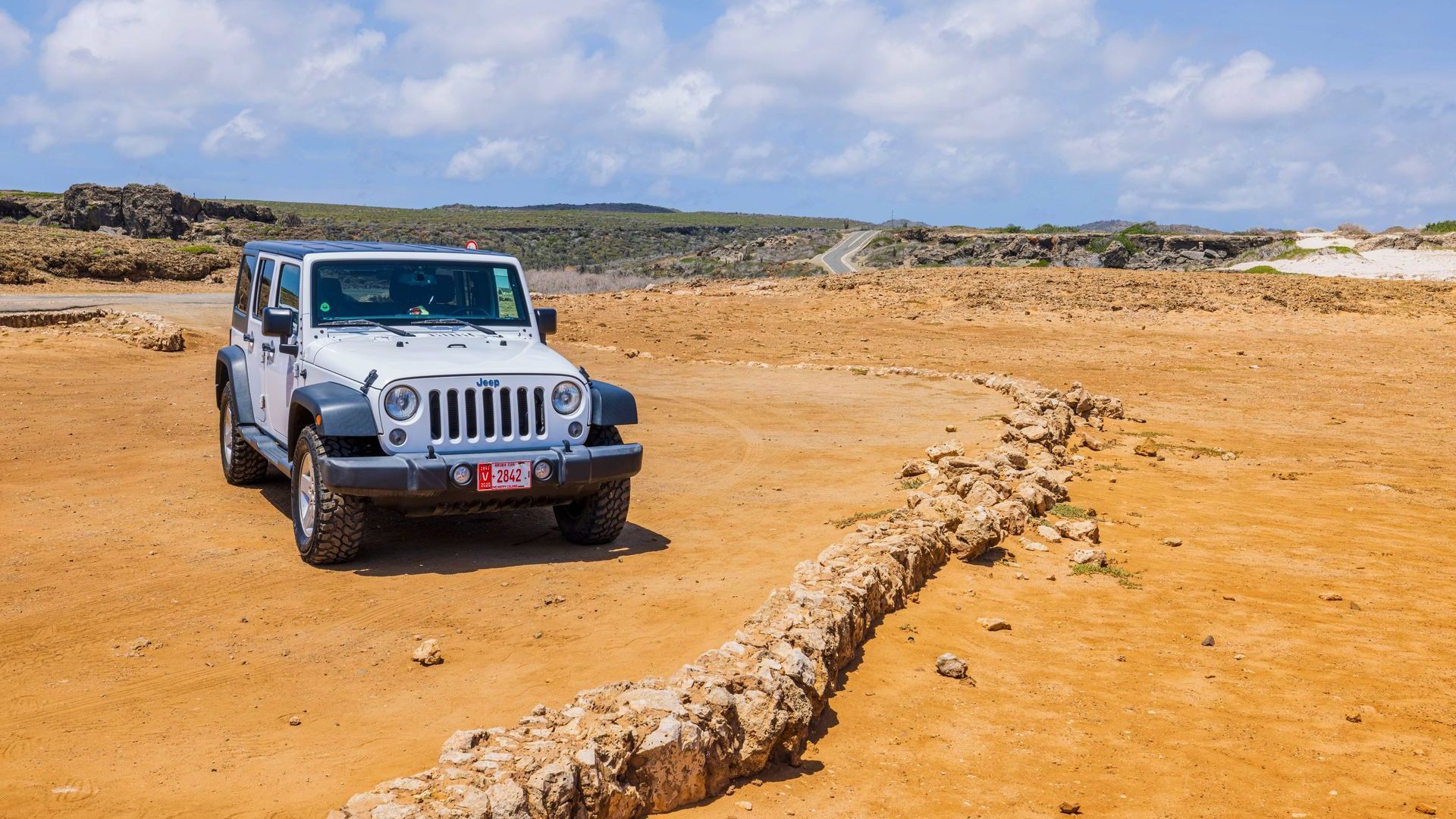 A white jeep is parked in the middle of a dirt field.