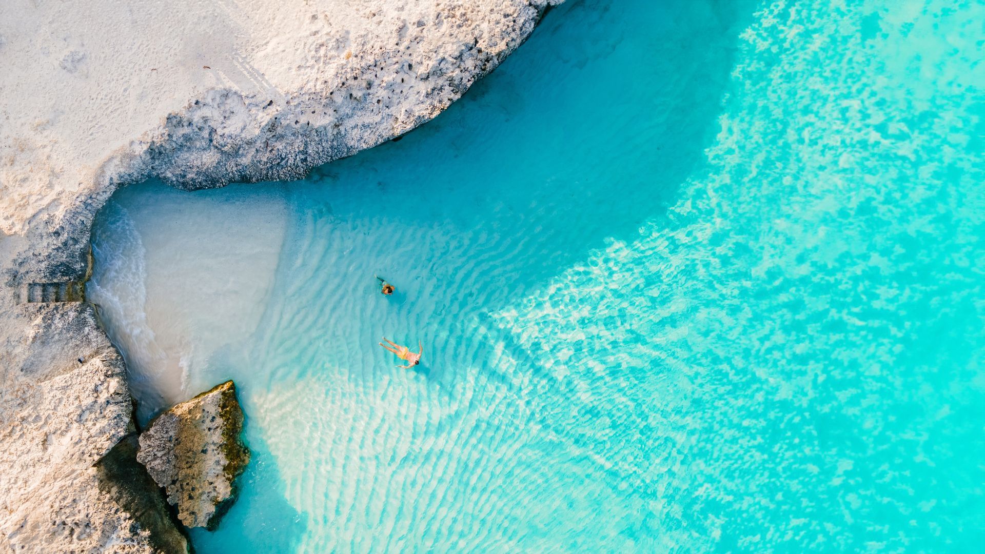 An aerial view of people swimming in a turquoise ocean.