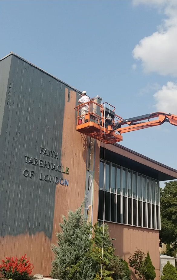 A man is painting the side of a building with a crane.