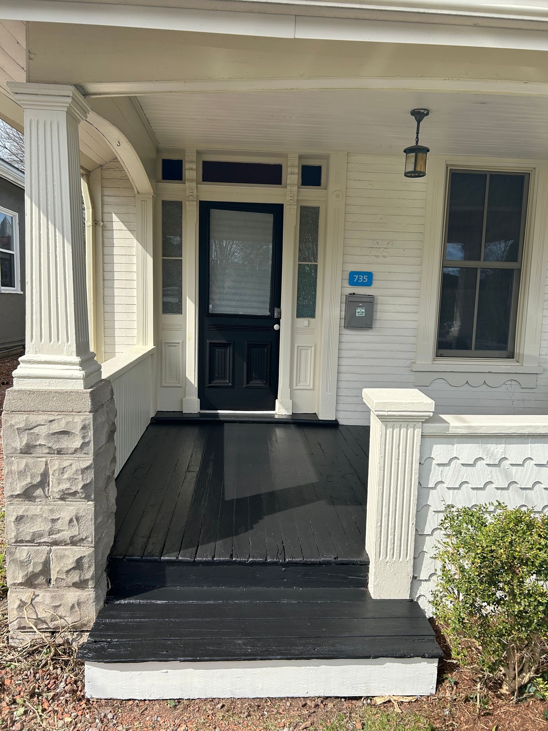 The front porch of a white house with a black door.