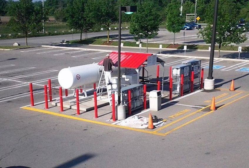A man is painting a propane tank in a parking lot