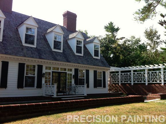 A white house with black shutters is being painted by precision painting
