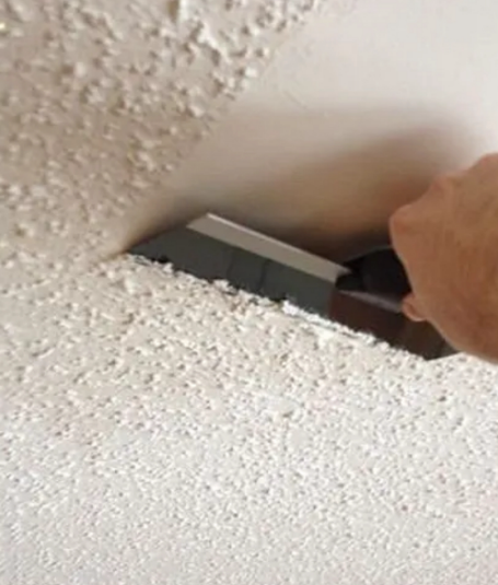 A person is using a spatula on a white wall.