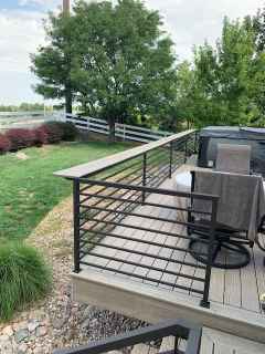 A deck with a railing and chairs and a hot tub in the background.