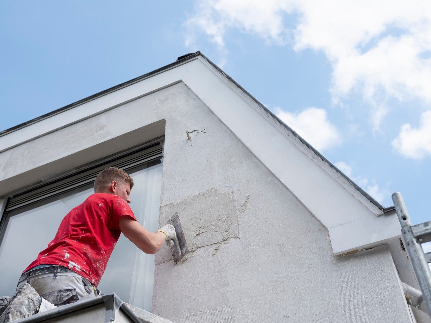 un uomo sta intonacando la facciata di un edificio con una cazzuola.