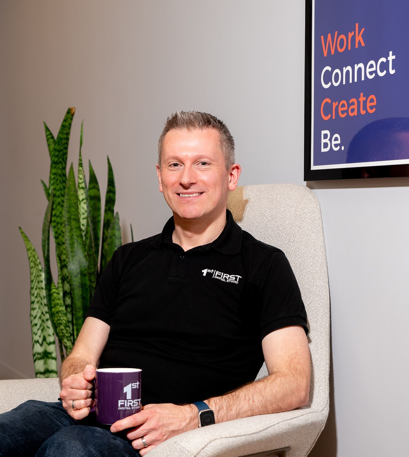 A man in a black shirt is sitting in a chair holding a cup of coffee.