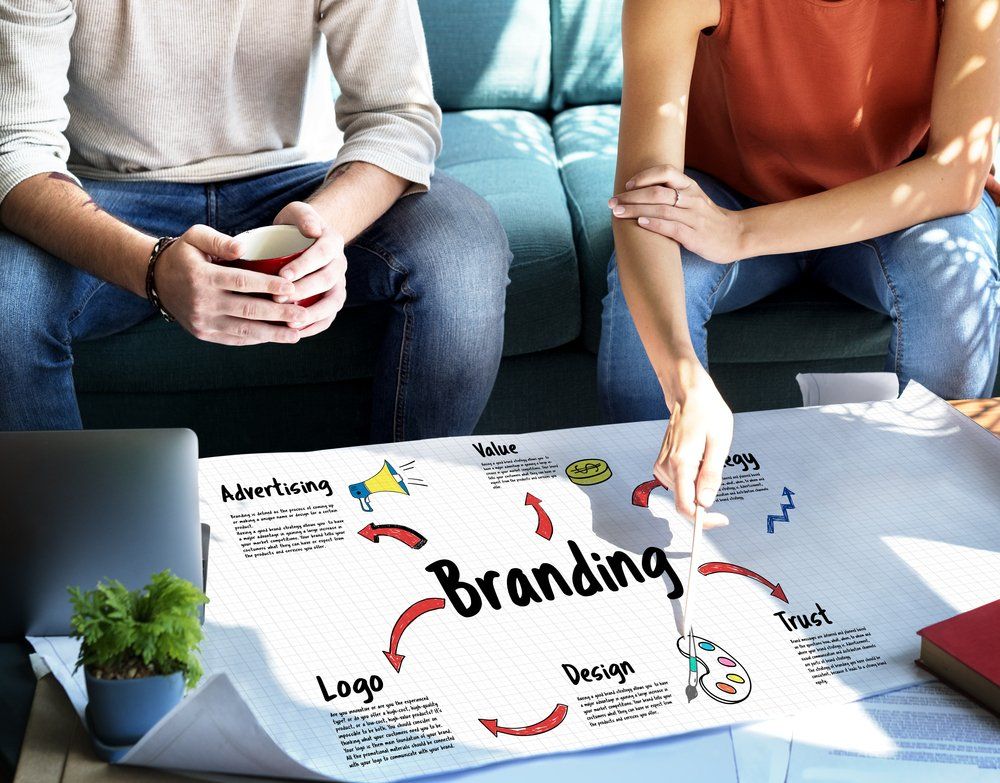 A man and a woman are sitting on a couch looking at a poster about branding.