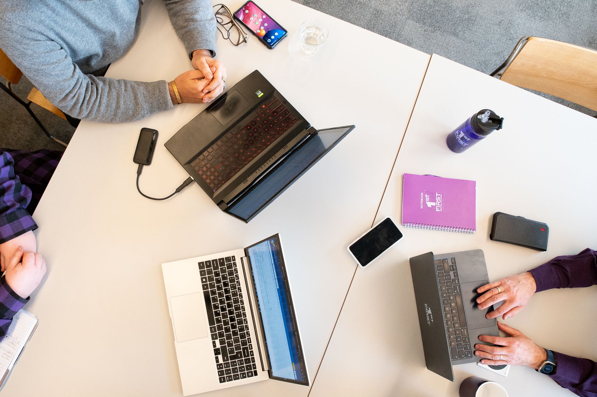 a purple notebook with the words First Digital Studio on it sits on a table with 3 laptops displaying digital marketing reports