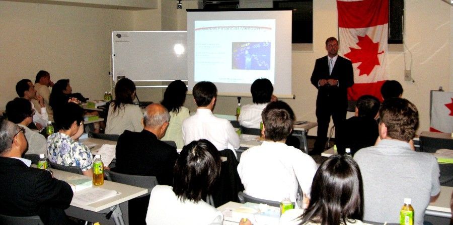 Allan Edwards, Canada Consul for Nagoya, giving a presentation to a seated audience, with a Canadian flag visible.