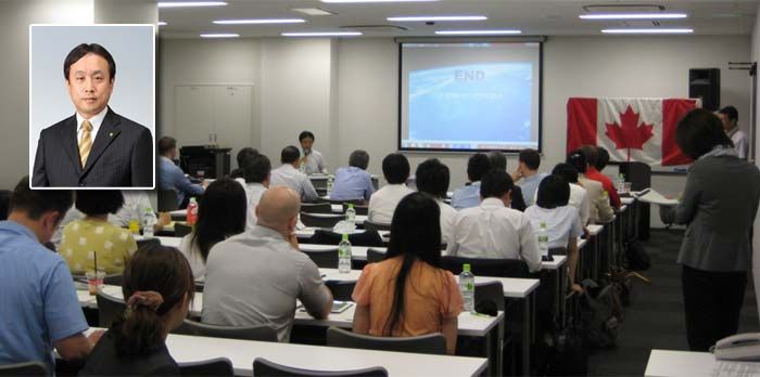 A classroom setting with a presenter at the front and attendees seated at desks.  A Canadian flag is displayed. A headshot is inset.
