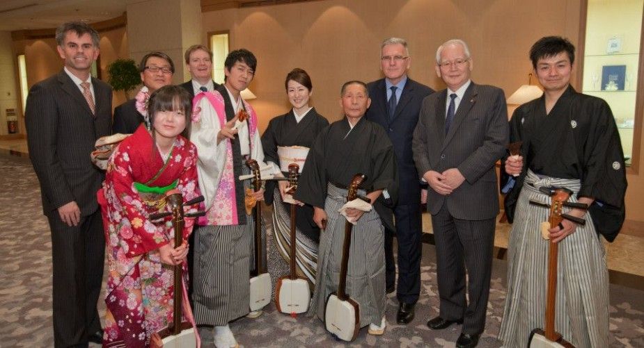 Group of people, some in suits, some in traditional Japanese attire, holding shamisen instruments.