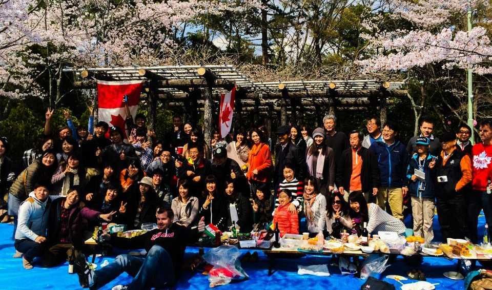 Group photo under cherry blossoms; people are smiling, and a Canadian flag is visible.