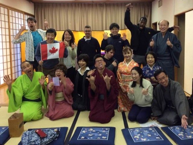 Group of people in traditional Japanese room, posing. Some wear kimonos, many smile and gesture.