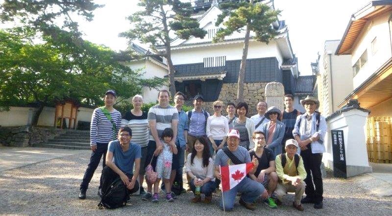 Group of people posing with a Canadian flag in front of a traditional Japanese building.