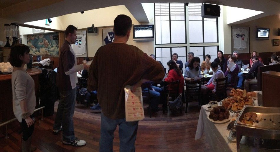 People gathered in a restaurant, some listening to a presentation. Food on a buffet table.