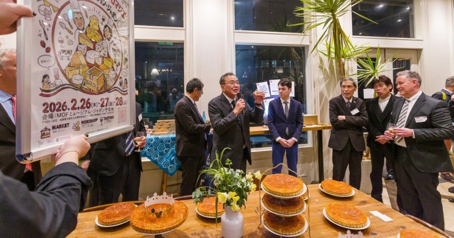 Group of men in suits at a gathering; holding a poster and cakes on a table.