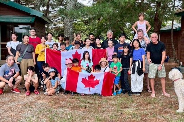 Group of people with a Canadian flag in front of cabins in a forest.