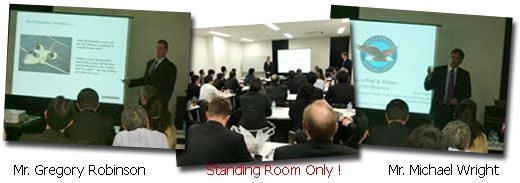 A packed conference room with two men giving presentations. 