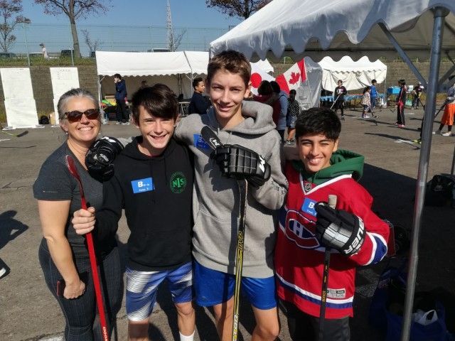 Woman and three boys in hockey gear pose outside, holding hockey sticks.