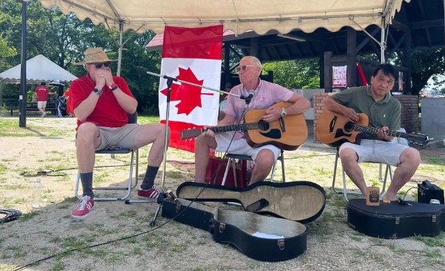 Three men are playing guitars in front of a Canadian flag