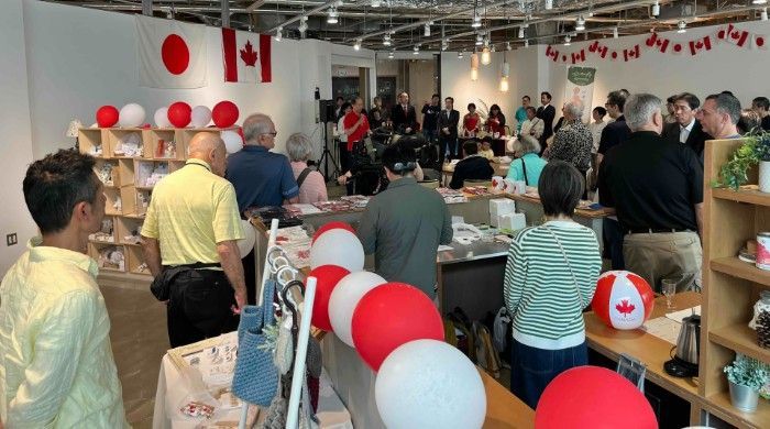 Crowded indoor event with red and white Canadian flags, balloons, and people browsing tables and shelves