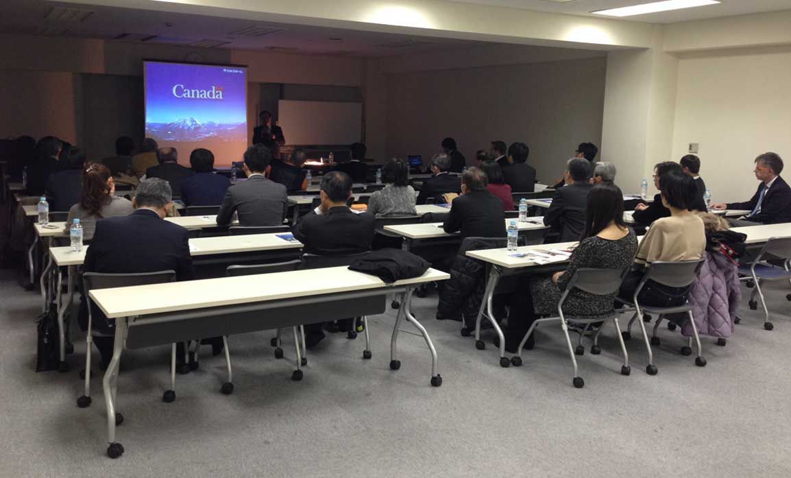 Audience at a presentation. A woman speaks at a screen with the word