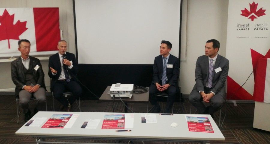 Panel discussion at an event with four men seated at a table. Canadian flags are visible.