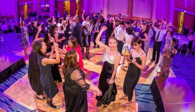 紫と金色の照明に照らされたパーティーの模様のあるダンスフロアで踊る人々。