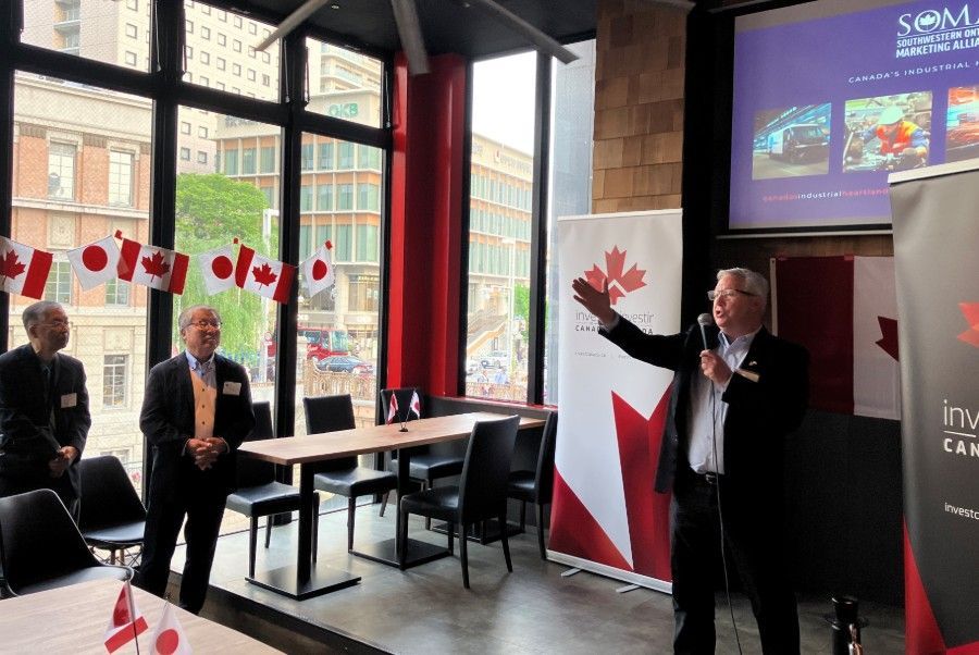 A man is giving a presentation in a room with a Canadian flag on the wall.