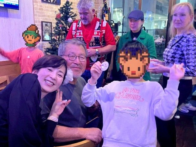 Group of people smiling, some with pixelated faces, indoors with Christmas decorations.