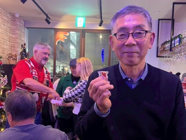 Man holding a small glass, smiling at a social gathering in a restaurant.