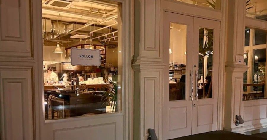 Restaurant exterior with white doors and window, interior tables visible, evening.