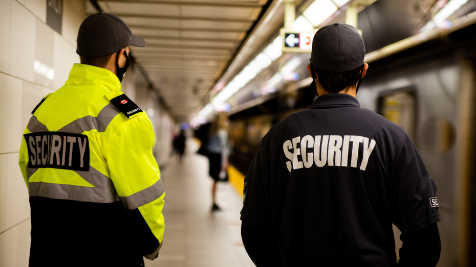 two security guards are standing next to each other at a train station .