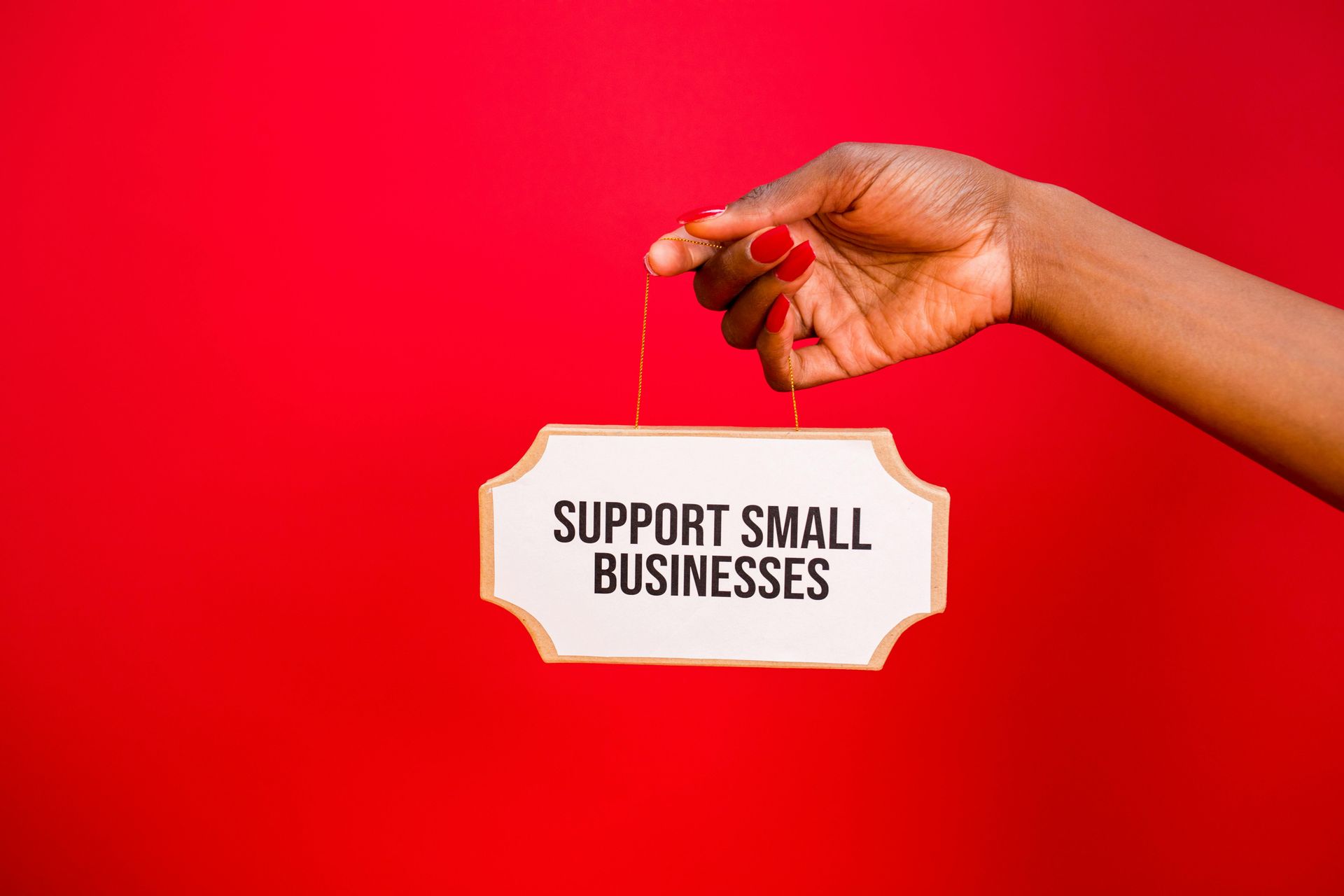 Hand holding a sign that says “Support Small Businesses” against a red background