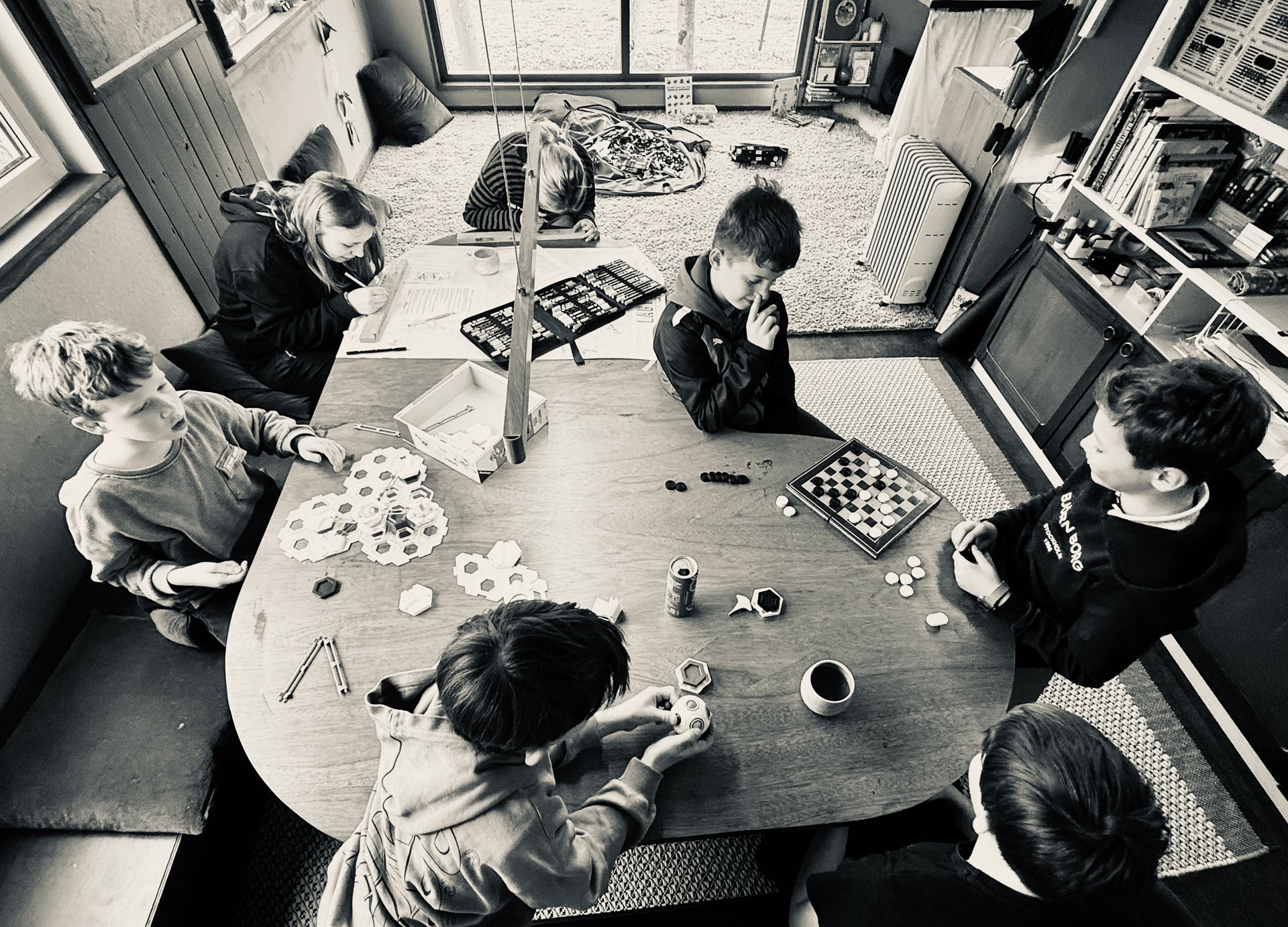 Een groep kinderen zit rond een tafel met een vrouw in het midden.