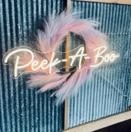 “Peek-A-Boo” neon sign with pastel pink and blue feathers on a blue corrugated wall