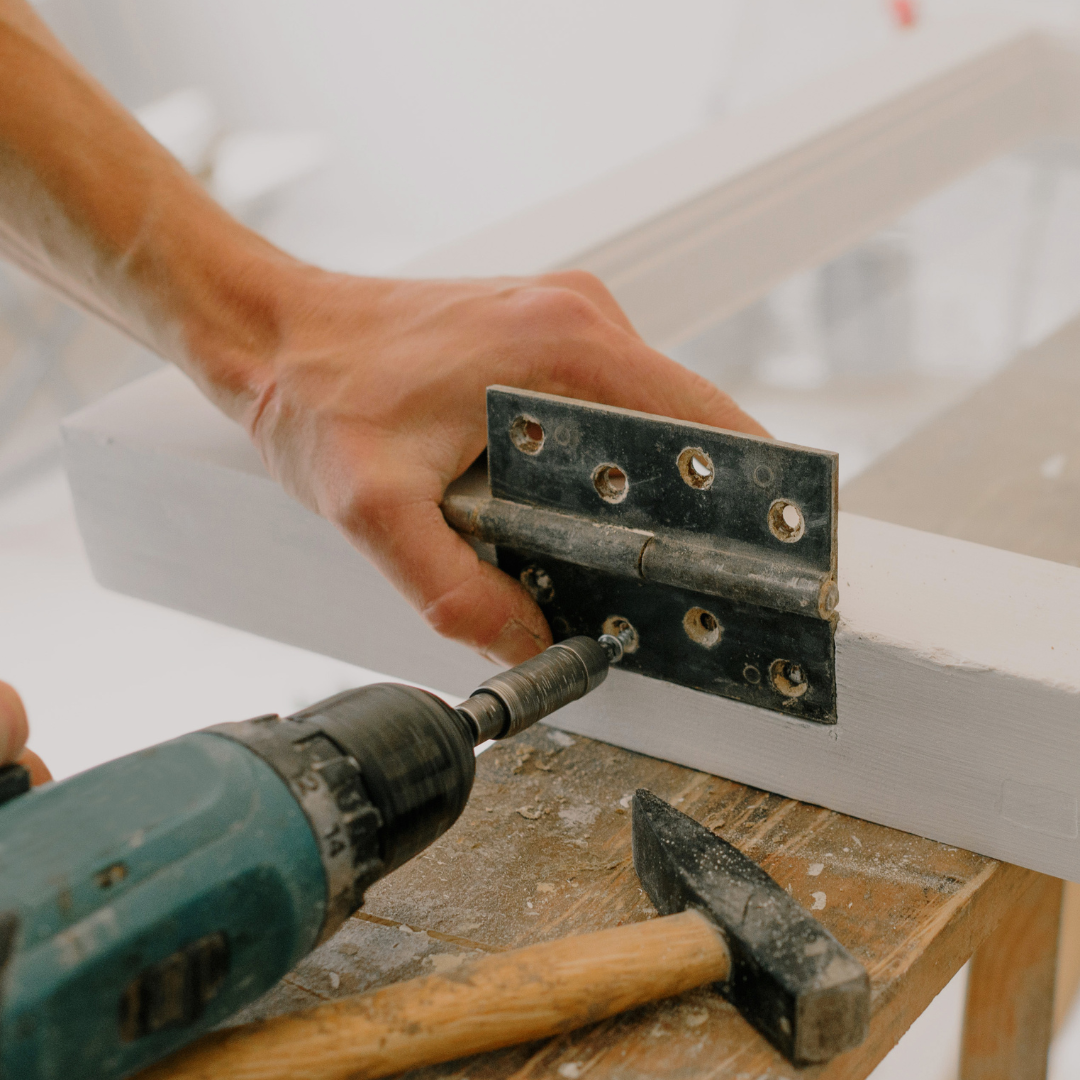 A person is using a drill to fix a door hinge.