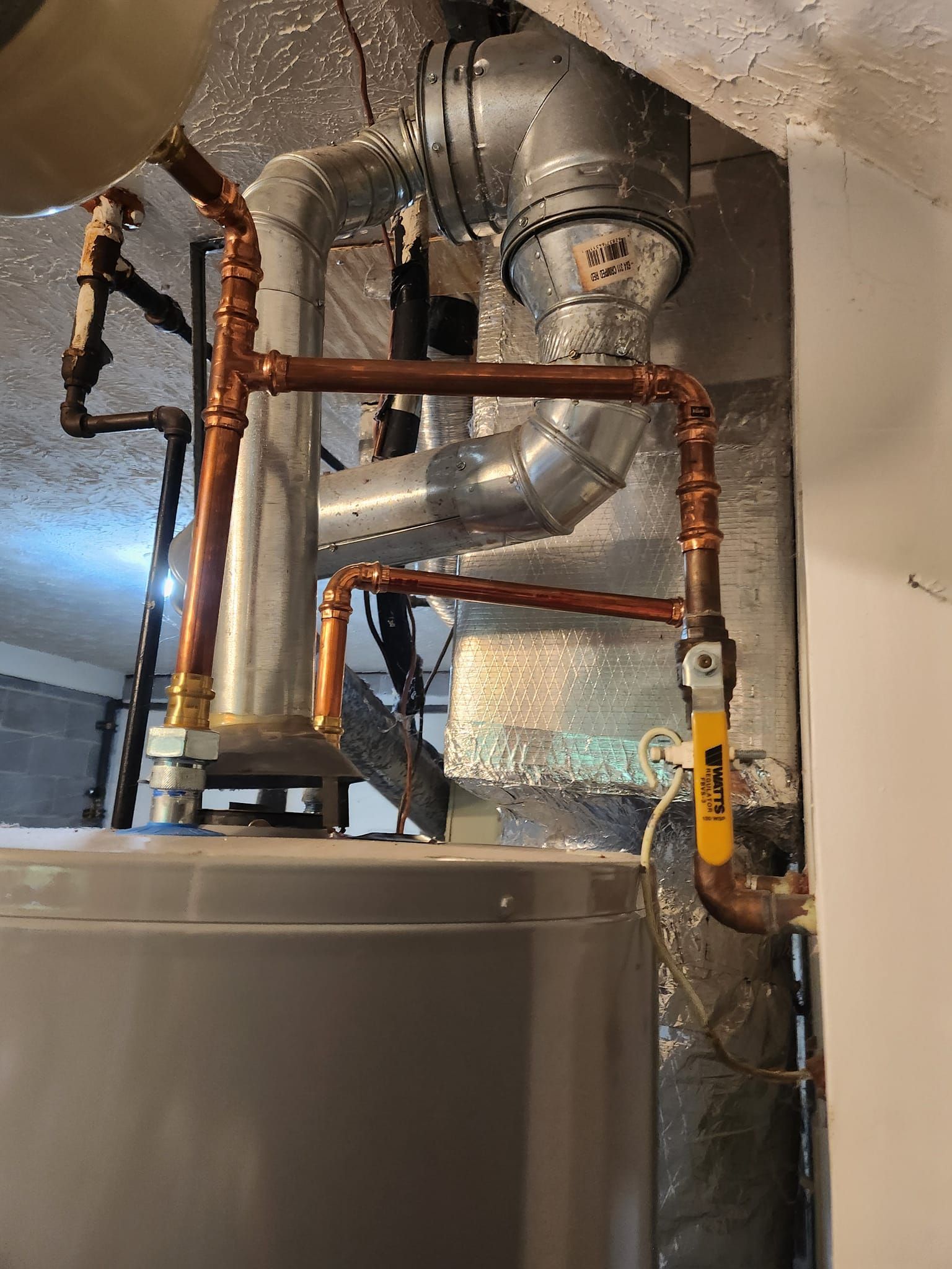 A close up of a water heater with copper pipes and a yellow valve.