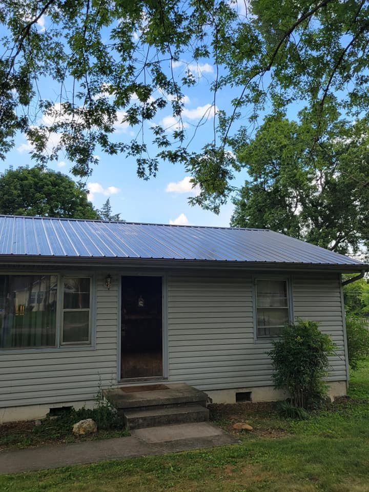 A small house with a metal roof is surrounded by trees.