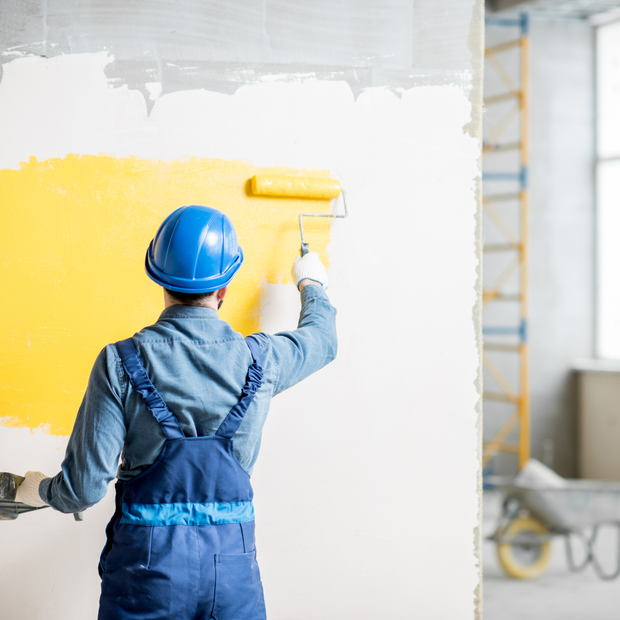 A man is painting a wall yellow with a roller.