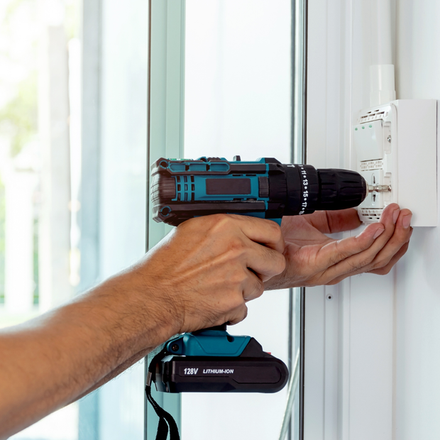 A man is using a cordless drill to install a light switch on a wall.