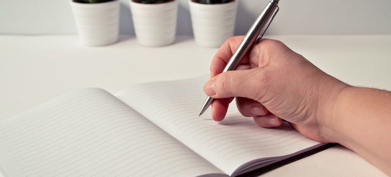 A person holding a pen and preparing to write something in a notebook.