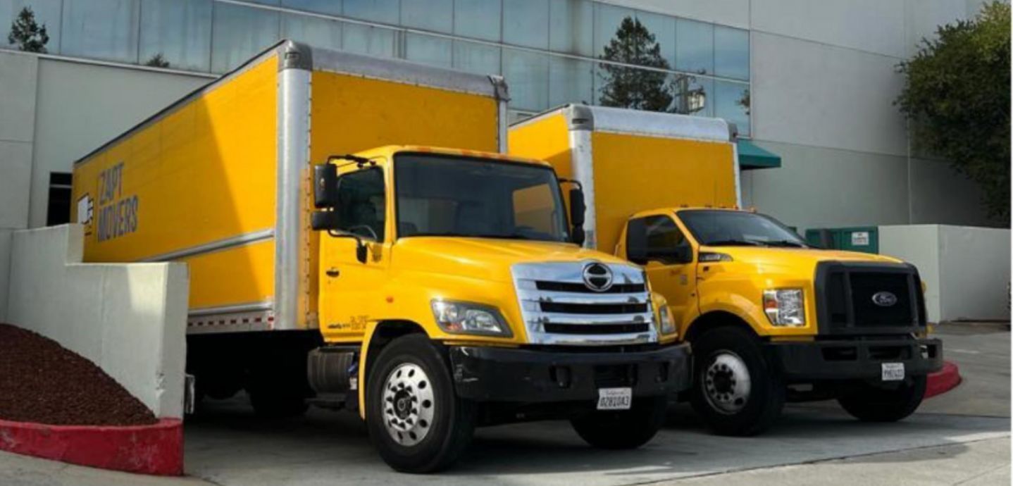 Two yellow trucks are parked next to each other in front of a building.