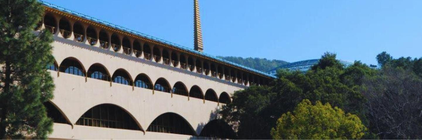 A large building with arches and a chimney on top of it is surrounded by trees.