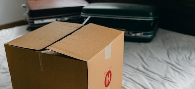 A moving box on a bed with two suitcases in the background