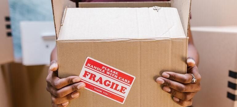 A person holding a moving box that is labeled as fragile