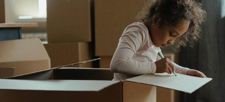 A little girl inside a big moving box and she draws on it