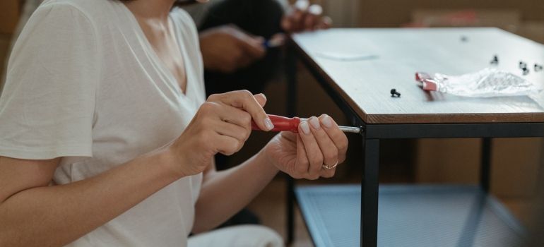 Woman holding screwdriver and assembling the table. 