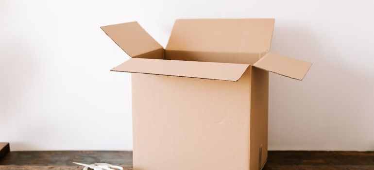 An open cardboard box is sitting on a wooden floor next to a white wall.