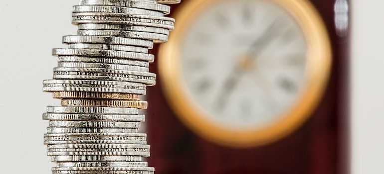 A stack of coins is sitting in front of a clock.